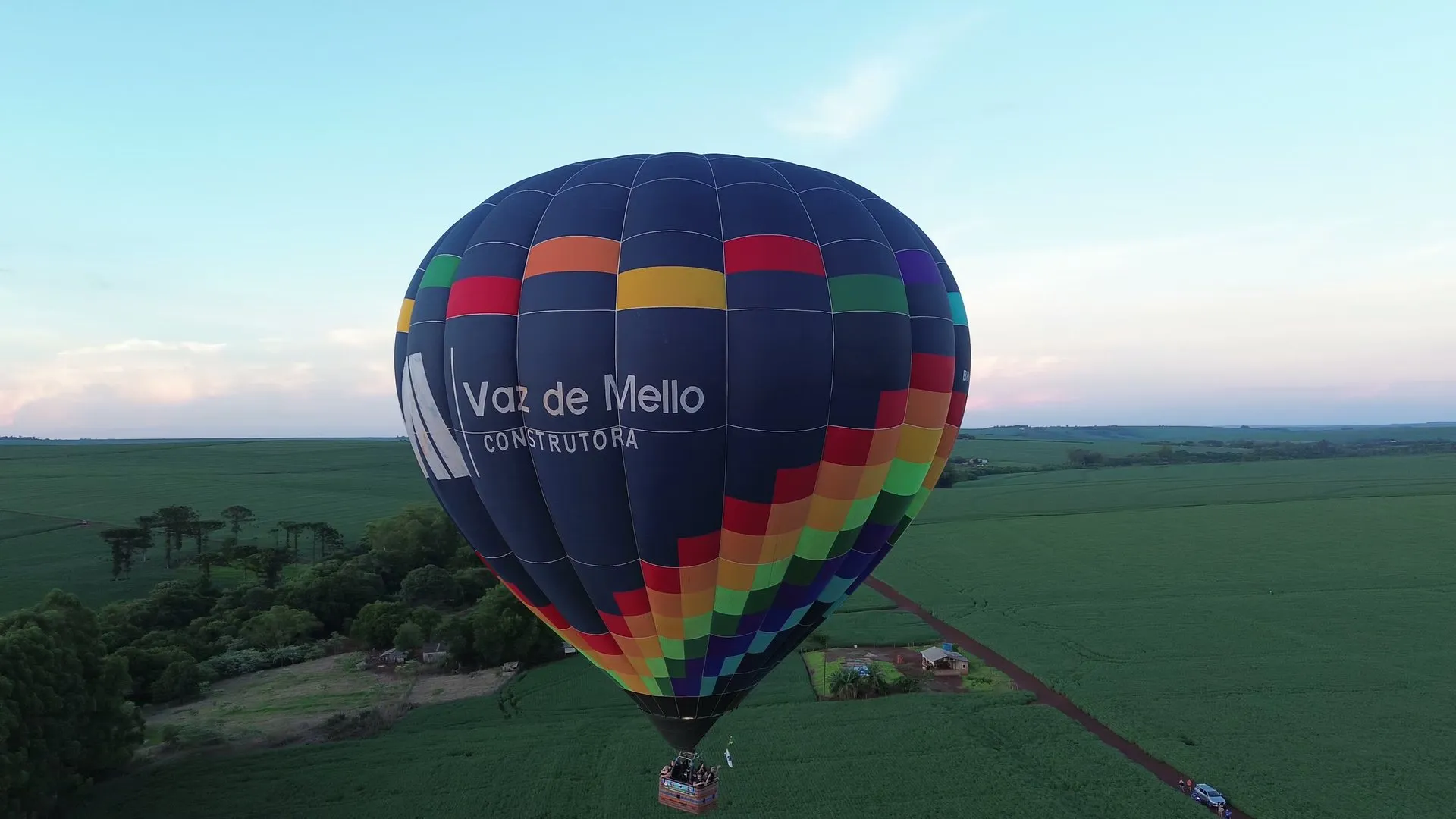 Balão com a marca Vaz de Mello Construtora voando sobre a mata e as lavouras